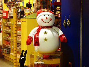 photo of a white snowman dressed in a red and white hat, red scarf, red mittens in a store window advertising a store closing sale